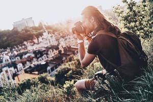 capturando uma bela vista. jovem em roupas casuais fotografando a vista enquanto está sentado na colina ao ar livre foto