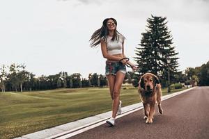 correndo com o amigo. comprimento total de mulher jovem e bonita brincando com seu cachorro e sorrindo enquanto corre ao ar livre foto