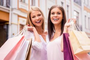 fazer compras juntos é divertido. duas mulheres jovens atraentes segurando sacolas de compras e sorrindo ao ar livre foto
