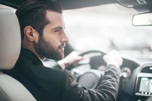 empresário no carro. vista traseira do jovem bonito olhando à direita enquanto dirigia um carro foto