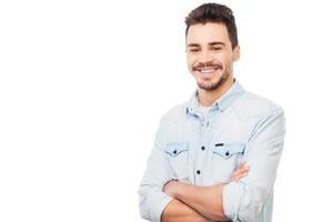 bonito e alegre. jovem bonito na camisa olhando para a câmera e mantendo os braços cruzados em pé contra um fundo branco foto