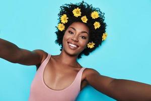 tirando selfie. autorretrato de mulher africana jovem e atraente olhando para a câmera e sorrindo enquanto estava deitado contra um fundo azul foto