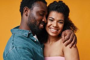 lindo jovem casal africano abraçando e sorrindo em pé contra um fundo amarelo foto