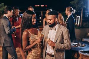 lindo jovem casal africano em trajes formais segurando taças de champanhe e sorrindo foto