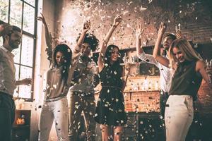 curtindo festa legal. grupo de jovens felizes jogando confete e pulando enquanto aproveita a festa em casa na cozinha foto