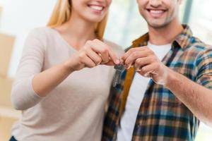 chaves do seu novo apartamento. imagem recortada de jovem casal apaixonado segurando as chaves e sorrindo em pé em sua nova casa foto
