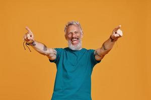 feliz homem sênior, mantendo os braços estendidos e sorrindo em pé contra um fundo laranja foto