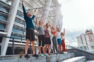 comprimento total de jovens em roupas esportivas, mantendo os braços estendidos e sorrindo em pé ao ar livre foto