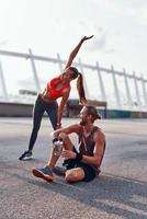 jovem e mulher em roupas esportivas aquecendo e esticando ao ar livre foto