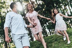 nada além da família. feliz jovem família de três de mãos dadas e sorrindo enquanto corre no parque foto