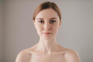 beleza Pura. retrato de mulher ruiva com sardas olhando para a câmera em pé contra um fundo cinza foto