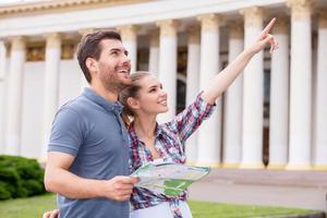 viajantes da cidade. feliz casal jovem turista em pé perto de belo edifício enquanto homem segurando mapa e mulher apontando para fora foto