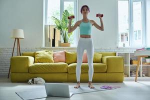 mulher jovem e bonita em roupas esportivas exercitando com halteres em casa foto