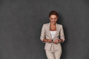 simplesmente feliz. mulher jovem e atraente em roupas casuais inteligentes sorrindo em pé contra um fundo cinza foto