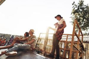 dia perfeito para patinar. grupo de jovens modernos saindo juntos enquanto passam o tempo no parque de skate ao ar livre foto