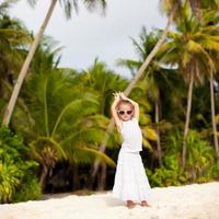 adorável garotinha em um vestido branco longo em uma praia tropical