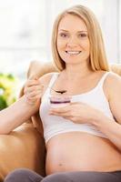 mulher grávida sonhando. mulher grávida feliz sentada na cadeira e comendo iogurte foto
