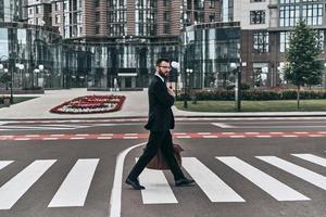 sempre cuidadoso. comprimento total de jovem de terno completo atravessando a rua enquanto caminhava ao ar livre foto