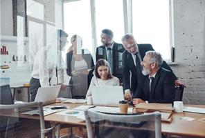 equipe de negócios autônoma analisando as vendas usando tecnologias modernas e sorrindo enquanto a equipe se reúne na sala da diretoria foto