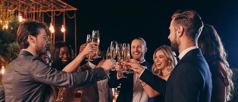 grupo de pessoas bonitas em trajes formais brindando com champanhe e sorrindo enquanto passa o tempo na festa de luxo foto