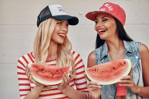 diversão de melancia. duas mulheres felizes segurando fatias de melancia e olhando uns aos outros em pé ao ar livre foto