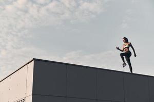 fitness é o modo de vida. comprimento total da jovem moderna em roupas esportivas pulando enquanto exercitava o tempo no telhado ao ar livre foto