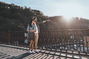 o amor os inspira. comprimento total de homem bonito abraçando uma jovem mulher atraente e apontando para fora em pé na ponte ao ar livre foto