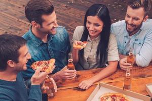 hora da pizza. vista superior de cinco pessoas alegres segurando garrafas com cerveja e comendo pizza ao ar livre