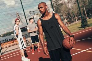 pensando no sucesso. jovem africano em roupas esportivas olhando para longe enquanto joga basquete ao ar livre foto