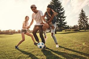 sentindo-se livre com os amigos. comprimento total de jovens sorridentes em roupas casuais correndo enquanto jogava futebol ao ar livre foto