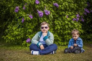 um menino posa perto de um lilás exuberante. retrato de crianças com uma expressão facial interessante. interações. foco seletivo. foto