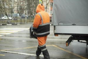 trabalhador coloca carga em transporte. roupas laranja para o trabalho. estrada de limpeza. foto