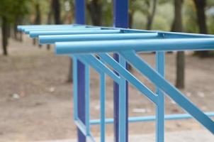 tubos de metal azul e barras transversais contra um campo de esportes de rua para treinamento de atletismo. equipamento de ginástica esportiva ao ar livre. foto macro com foco seletivo e fundo extremamente desfocado