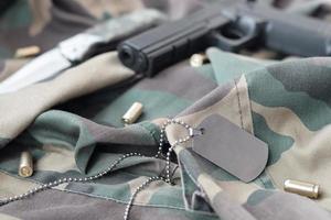 token de etiqueta de cão do exército com balas de 9 mm e pistola em tecido verde de camuflagem dobrado foto