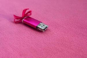 cartão de memória flash usb rosa brilhante com um laço rosa encontra-se em um cobertor de tecido de lã rosa claro macio e peludo. design de presente feminino clássico para um cartão de memória foto