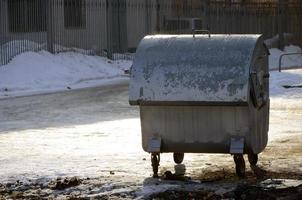 um recipiente de lixo prateado fica perto de edifícios residenciais no inverno foto