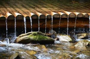 drenos de água de madeira feitos à mão de pequenas vigas tratadas. um belo fragmento de uma pequena cachoeira foto