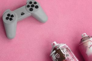 adolescentes e conceito de estilo de vida da juventude. joystick e duas latas de spray estão no cobertor de tecido de lã rosa peludo. controladores para videogames e latas de tinta em um fundo de material de lã de pelúcia foto