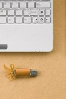 cartão de memória flash usb laranja com um laço está em um cobertor de tecido de lã laranja claro macio e peludo ao lado de um laptop branco. design de presente feminino clássico para um cartão de memória foto