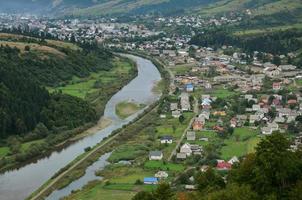 uma bela vista da vila de mezhgorye, região dos cárpatos. muitos edifícios residenciais cercados por altas montanhas da floresta e longo rio foto