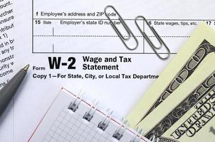 a caneta, o caderno e as notas de dólar estão no formulário de imposto w-2 salário e declaração de imposto. hora de pagar impostos foto