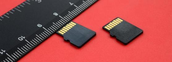 dois pequenos cartões de memória micro SD estão sobre um fundo vermelho ao lado de uma régua preta. um armazenamento de dados e informações pequeno e compacto foto