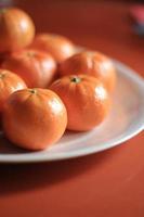 pequenas laranjas são colocadas em um prato branco na mesa laranja. foto