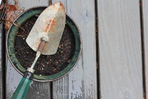 uma pequena pá é colocada em um vaso de plantas ao fundo como uma varanda de madeira encharcada de chuva. foto