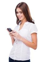 mandando mensagem para ele. mulheres bonitas segurando o celular e sorrindo em pé contra um fundo branco foto