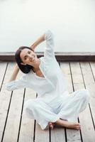 treinando seu corpo e alma. bela jovem sorridente em roupas brancas realizando ioga ao ar livre foto