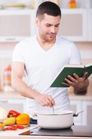 tinha um gosto tão bom jovem bonito provando sopa da panela e sorrindo em pé na cozinha foto