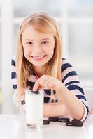 mergulhando um biscoito. menina bonitinha mergulhando biscoito no leite e sorrindo foto