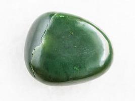 pedra preciosa de nefrite verde caída em mármore branco foto