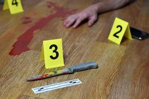 investigação da cena do crime - faca ensanguentada e mão das vítimas com marcadores criminais amarelos no chão da cozinha foto